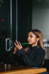 A portrait of a beautiful, young and attractive Asian woman manager, professional or entrepreneur in a business suit putting on foundation, mascara and blusher before her business meeting.
