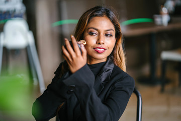 A portrait of a beautiful, young and attractive Asian woman manager, professional or entrepreneur in a business suit putting on foundation, mascara and blusher before her business meeting.