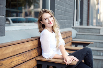 Attractive young woman in vintage jeans sitting on a chair in an outdoor restaurant. Attractive...