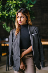 Portrait of a fashionable, capable and confident Southeast Asian woman in the city during the day. She is young, attractive and wearing a black turtleneck, khakis and has a jacket over her shoulders.