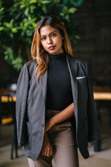 Portrait of a fashionable, capable and confident Southeast Asian woman in the city during the day. She is young, attractive and wearing a black turtleneck, khakis and has a jacket over her shoulders.