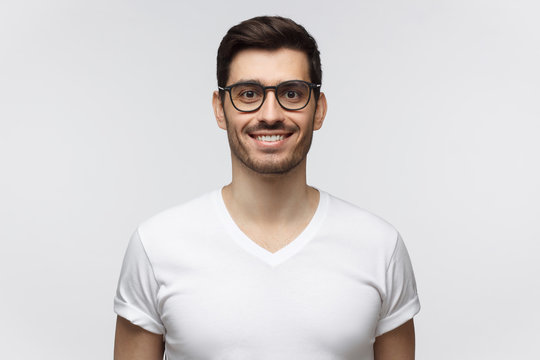 Smiling handsome young man in white t-shirt, looking at camera, isolated on gray background