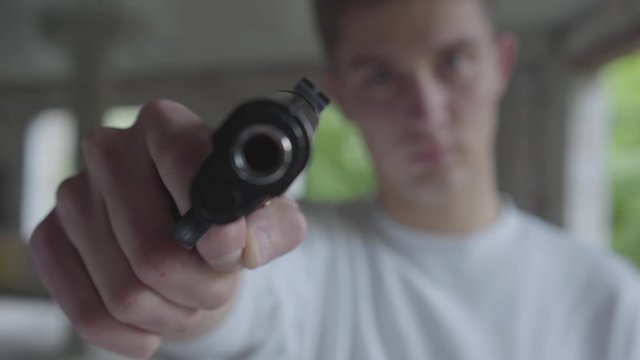Young man aiming with the pistol, his hands shaking close-up. The guy is going to kill the human in an abandoned building
