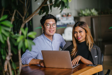 Portrait of a two young and confident professional Asian business people sitting in a cafeteria the...