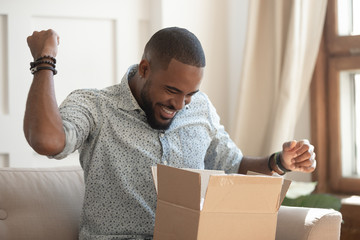 Excited african man customer receive open parcel box at home - Powered by Adobe