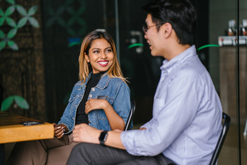 A two young business colleagues is having a meeting in a trendy coworking office. They are smiling and seem to be having fun together.