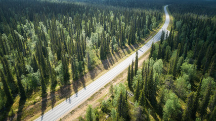Aerial view from above of country road through the green summer forest in Lapland. Beautiful fir...