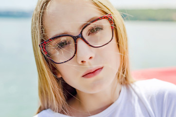 Fototapeta na wymiar Summer portrait of a blonde girl in glasses on a lake background. Close-up, focus to the foreground