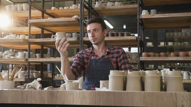 Male potter looking to the handmade cap during work day in the pottery.