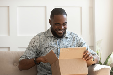Smiling african man consumer open cardboard box get postal parcel