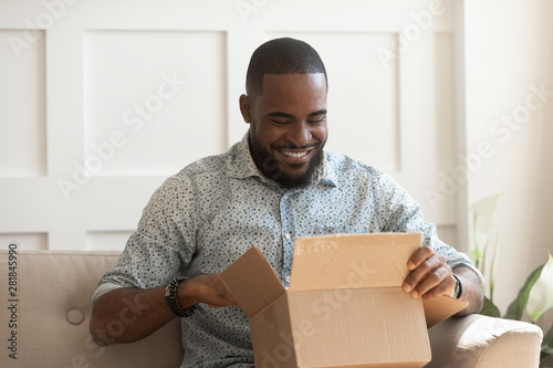 Smiling african man consumer open cardboard box get postal parcel