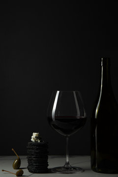 Wine and cheese, with crackers and caper berries on a marble tile surface.