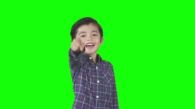 Little boy looks mocking someone by laughing and pointing at the camera in the studio. Shot in 4k resolution with green screen background