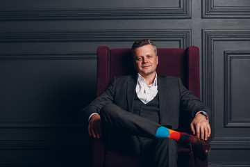 Portrait of sitting chair businessman in strict gray suit and colorful multi colored socks....