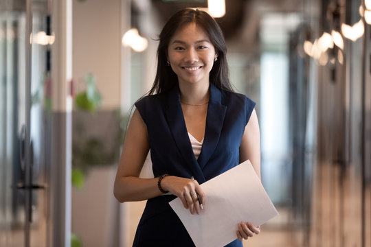 Happy asian businesswoman looking at camera stand in office hallway