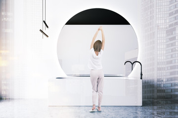 Fototapeta na wymiar Woman in white bathroom with tub and mirror