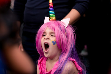 A cute girl is dressed up like a unicorn with a colorful wig, headband, ears, hooves and wings. 