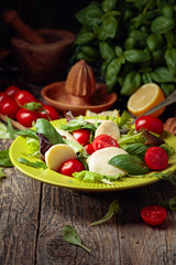 Green salad with mozzarella, tomato and basil in green plate on a old wooden background.