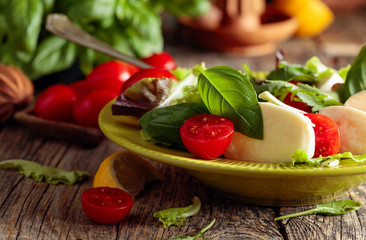Green salad with mozzarella, tomato and basil in green plate on a old wooden background.