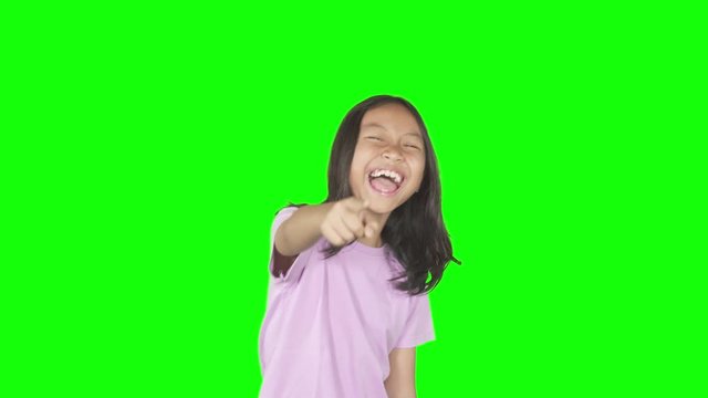 Female elementary school student looks mocking someone by laughing and pointing at the camera. Shot in 4k resolution with green screen background