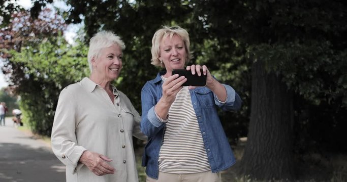 Mature lesbian couple taking selfie outdoors in summer