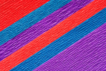 Abstract textured background of the close up detail of sheets of blue, purple and red crepe paper