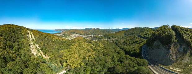 drone aerial view - summer cloudless day over a mountain pass. Narrow winding seaside road among wooded mountains.