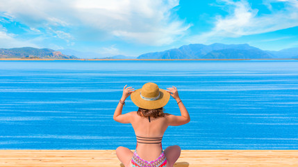 Fototapeta na wymiar Young girl in hat sunbathes on a wooden pier and summer landscape on the sea - Iztuzu beach, Turkey