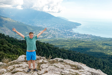 Obraz premium Young man standing on top of cliff in mountains and enjoying view of nature. Mountains and sea