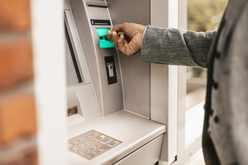 Close up shot of senior man hand using bank credit card. He typing pin code on keypad of ATM...