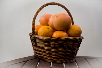 wicker basket with oranges and grapefruits on white background