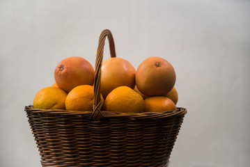 wicker basket with oranges and grapefruits on white background