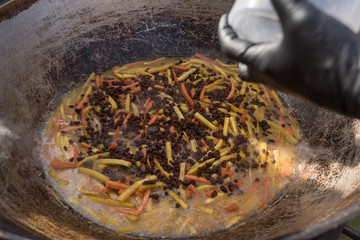 Cooking pilaf in a large cauldron on the street. Asian cuisine