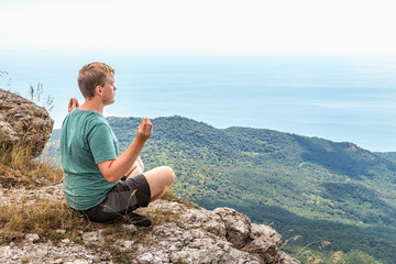Naklejka na ściany i meble Young man practicing yoga pose sitting on the rocky peak. Man do meditation and enjoying view