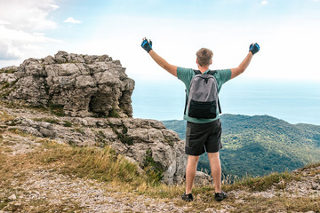 Young man with a backpack on top of cliff enjoying view of nature. Mountains and sea
