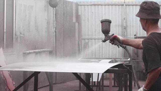 Old man worker applying anti-corrosion powder coating to metal sheet in slow motion. He is using spray gun in factory. Protection metal sheet from destruction.