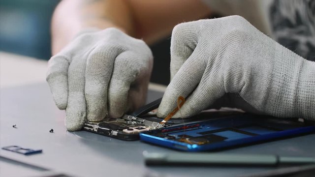 Technician disassembles mobile phone and looking for breakdowns. Professional repairman repairs smartphone removes details in workshop hands closeup. Electronics repair and maintenance service center.