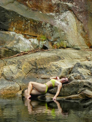 Young and sexy woman in a green swimsuit on a beautiful waterfall in the jungle