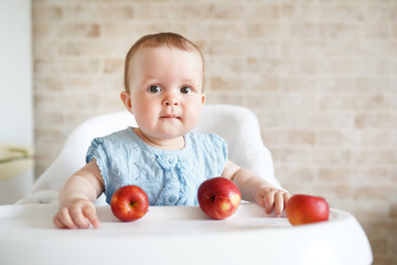 Fototapeta na wymiar Cute baby girl eating apple in the kitchen. Little kid tasting solids at home. Healthy nutrition for kids. copy space