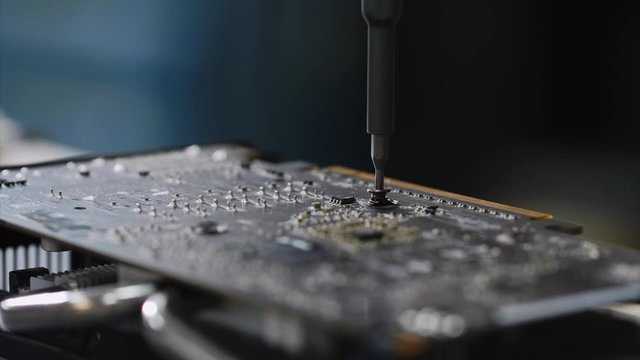 Master repairs of computer equipment, establishing chip and circuits. PC technician screws chipset of graphics card to ventilator installing it, hands closeup. PC repair and maintenance in workshop.