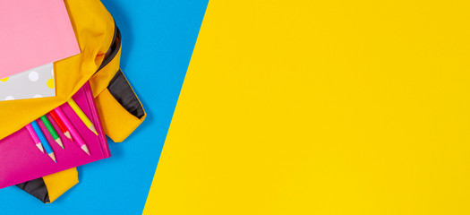 Back to school concept. Yellow backpack with school supplies on yellow and light blue background. Top view