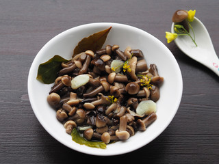 Excellent and beautiful pickled mushrooms and spices in a white plate, one fungus in a spoon on a wooden background.  Home recipe pickles - small mushrooms with garlic and herbs close-up.