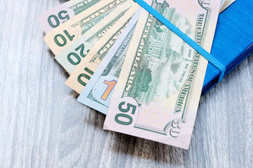 Money, dollars in a blue notebook with a blue ribbon. Background grey wooden surface. The concept of calculating the budget for the business, opening an account for payment.