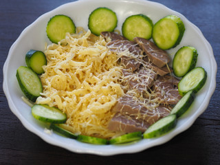 Pasta, grated cheese, boiled tongue and fresh cucumbers in a white plate on a dark table. Simple and delicious recipe to cook for lunch and dinner.