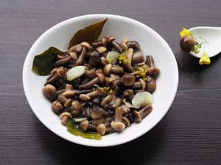 Delicious and beautiful pickled mushrooms and spices in a white plate, one fungus in a spoon on a wooden background.  Home recipe pickles - small mushrooms with garlic and herbs close-up.
