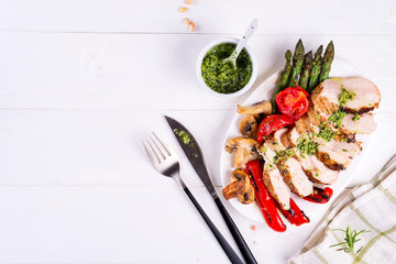 Grilled chicken breast on a plate with tomatoes, asparagus and mushrooms on a wooden background,...