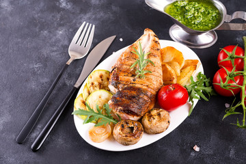 Grilled chicken breast on a plate with tomatoes, mushrooms and green sauce on a stone background, flat lay