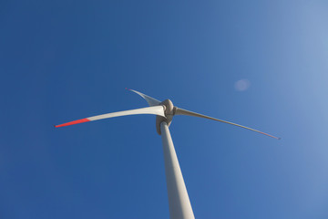 Fototapeta na wymiar wind turbine with sun flare blue sky background view from below