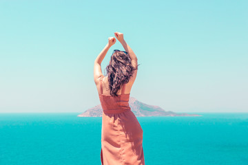 A young girl in a summer brown dress dancing on a background of blue sea, enjoying holiday and vacation