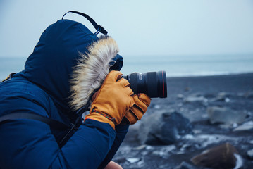 Photographer Takes picture on black sands beach with winter clothes.
